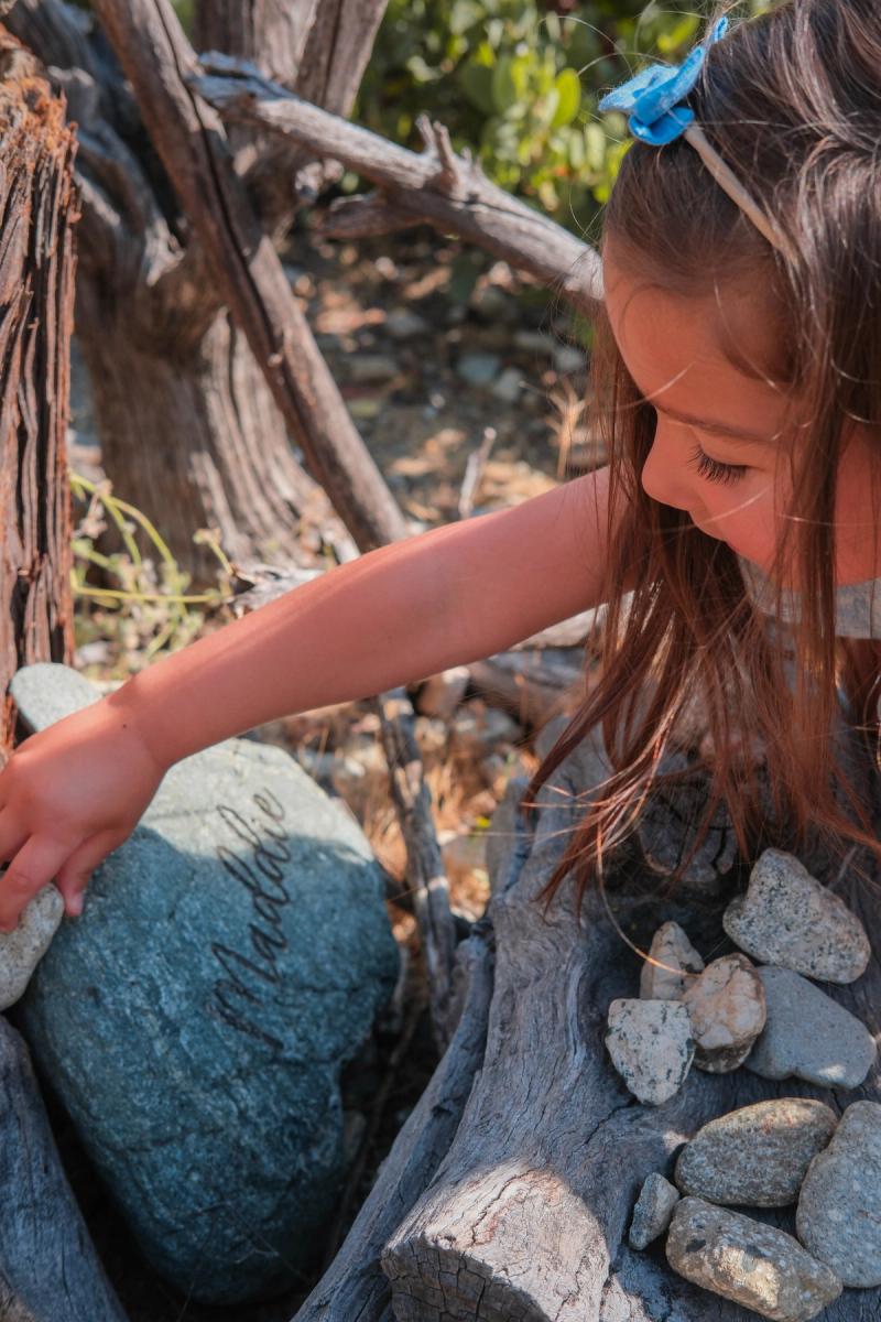Little girl in a blue bow touching a mossy stone by a garden fountain