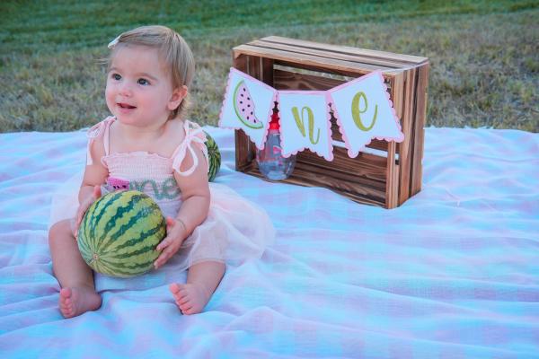 Birthday girl laughing on a gingham blanket next to a watermelon