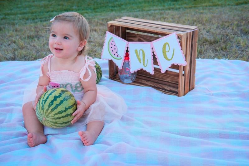 Birthday girl laughing on a gingham blanket next to a watermelon