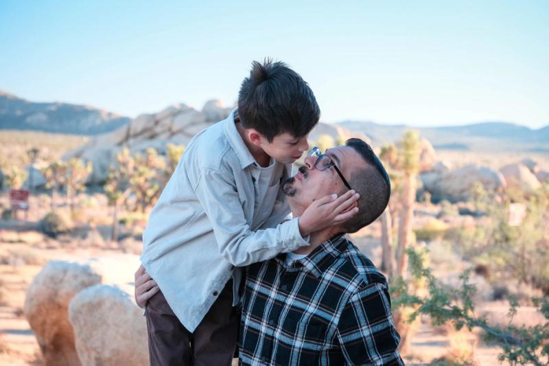 Son leaning in to kiss his dad's cheek with the desert behind them
