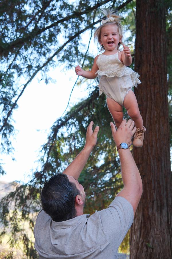 Dad lifting his daughter high toward the treetops