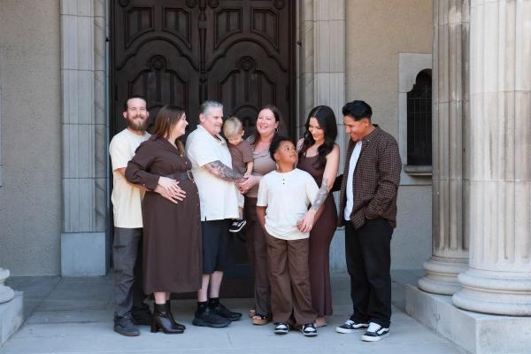 Extended family of eight in coordinated cream and brown outfits in front of tall carved wooden doors