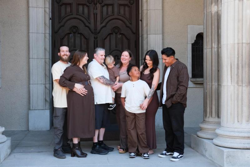 Extended family of eight in coordinated cream and brown outfits in front of tall carved wooden doors