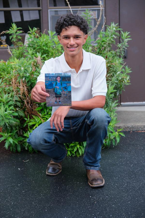 Teen crouching among the plants with a childhood photo in hand