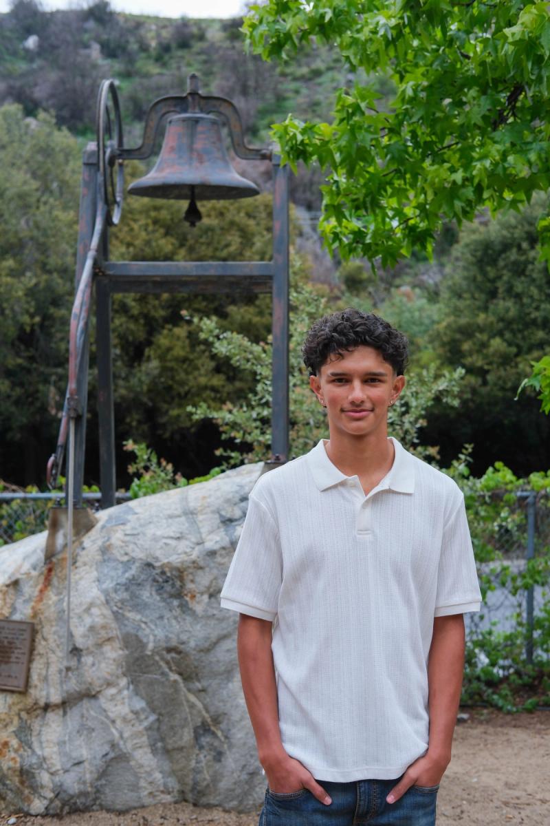 Teen standing in front of an old school bell on a boulder