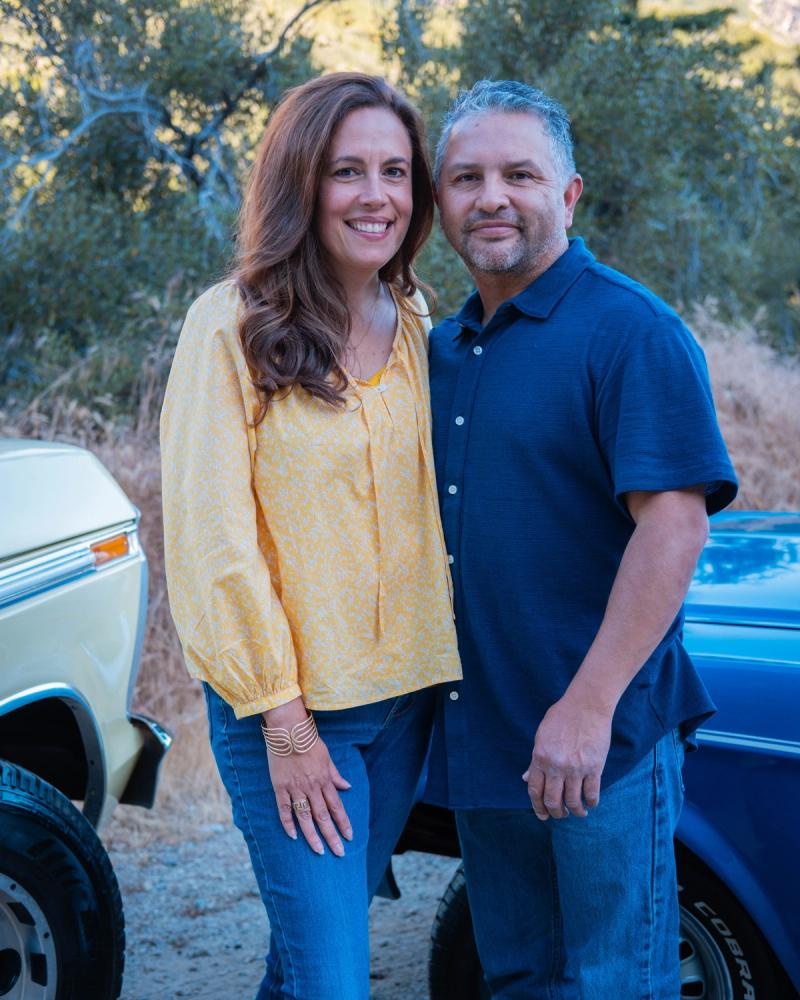 Couple standing arm in arm in front of their classic truck