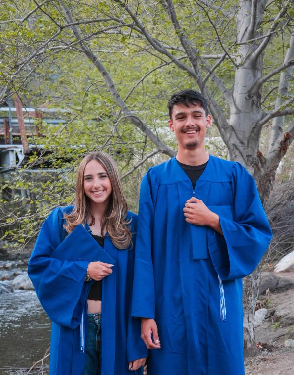 Brother and sister graduates in blue caps and gowns by a creek
