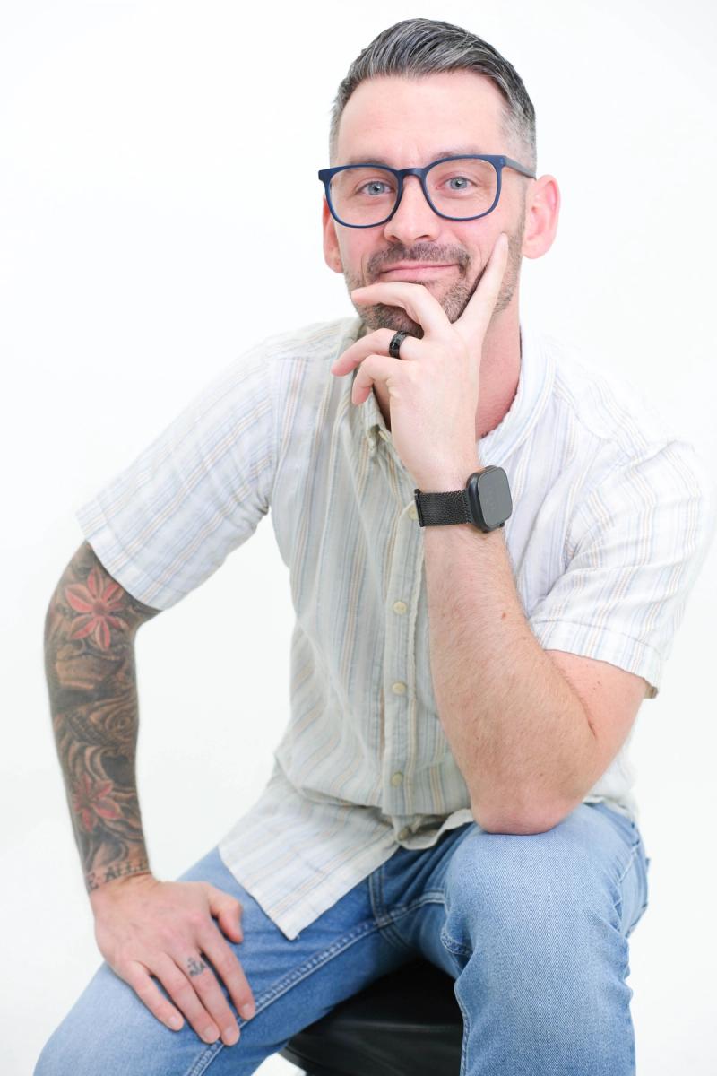 Man in glasses with a thoughtful expression, hand on his chin, seated in the studio