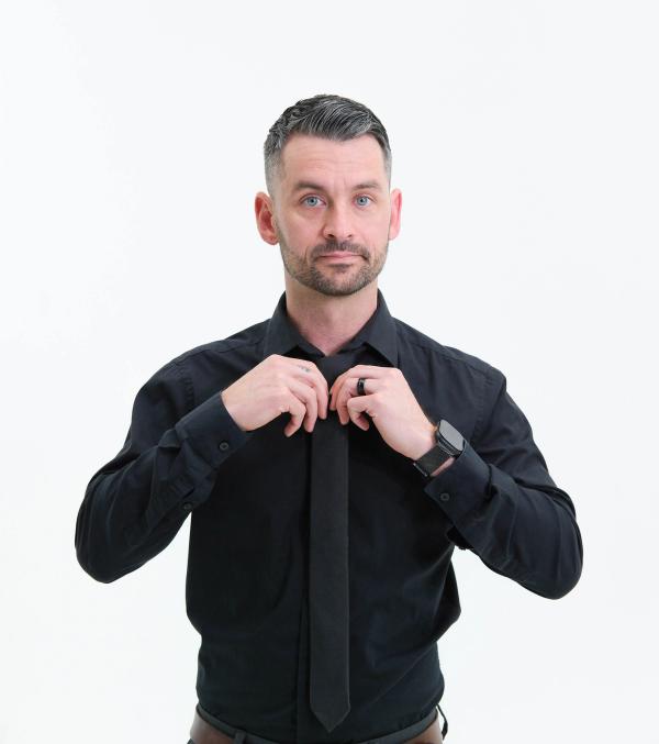 Man in a black shirt adjusting his tie, looking at the camera