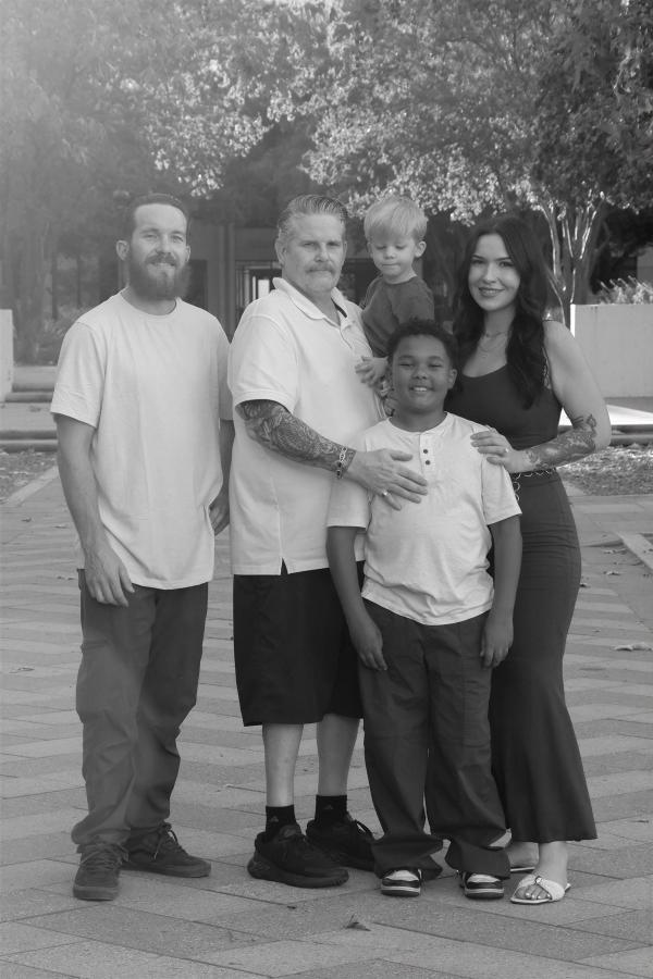 Black and white portrait of a family of five standing close under the trees