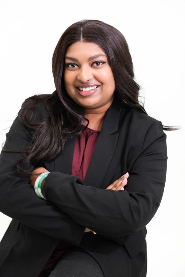 Seated woman in a black blazer and burgundy blouse with arms crossed