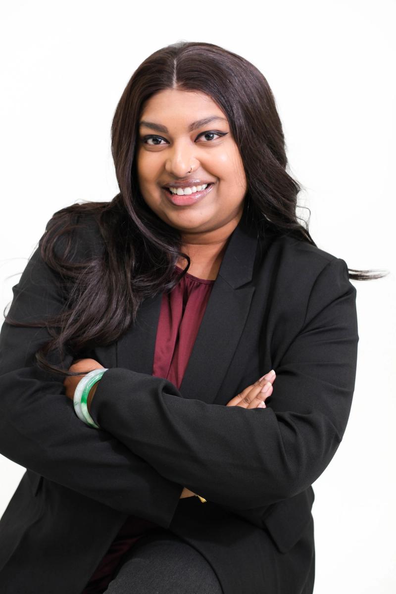 Seated woman in a black blazer and burgundy blouse with arms crossed
