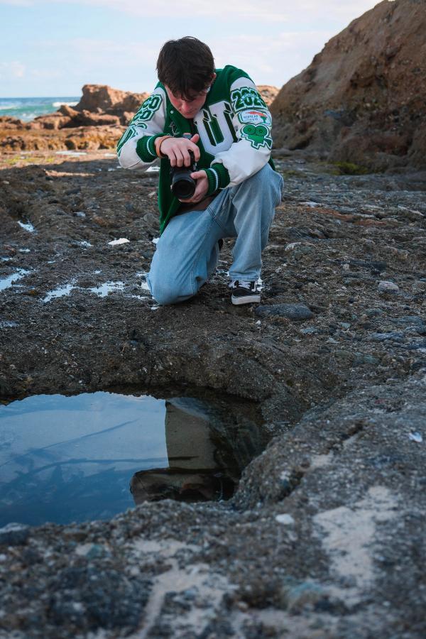 Senior crouched on the rocks photographing a tide pool