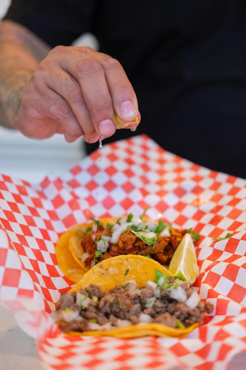 Hand squeezing lime over street tacos on red checkered paper