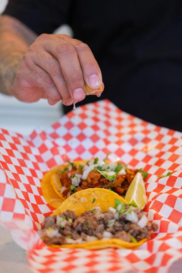 Hand squeezing lime over street tacos on red checkered paper