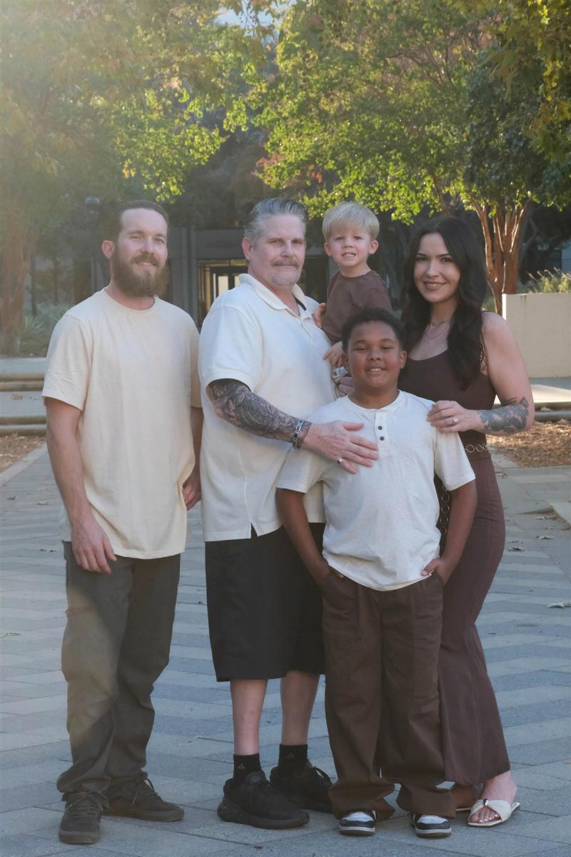 Family of five standing together under autumn trees, a toddler perched on grandpa's shoulders