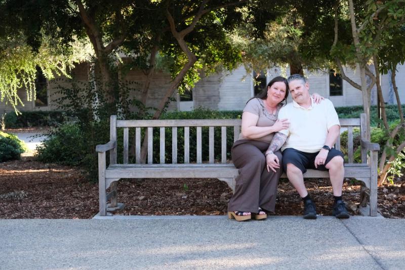 Older couple seated on a wooden bench in a leafy garden