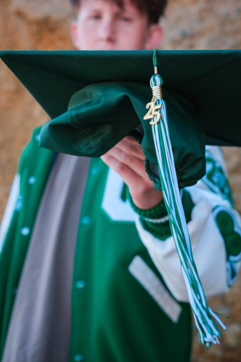 Graduate holding his cap so the 2025 tassel hangs in front of the camera