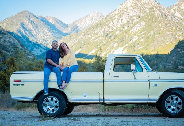 Couple sitting on the side of their pickup below a golden mountain