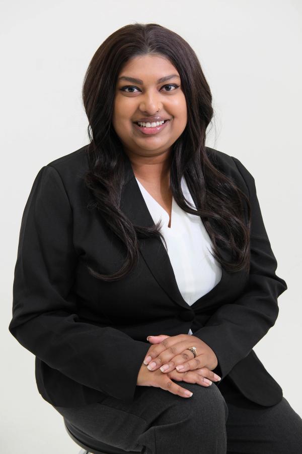 Woman in a black suit seated with hands resting on her knee