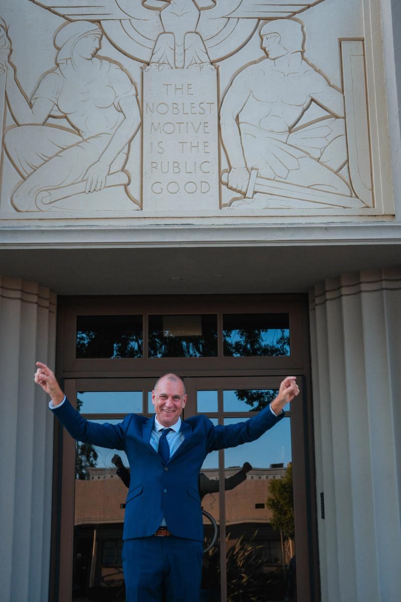 Candidate with arms raised in front of a carved civic doorway
