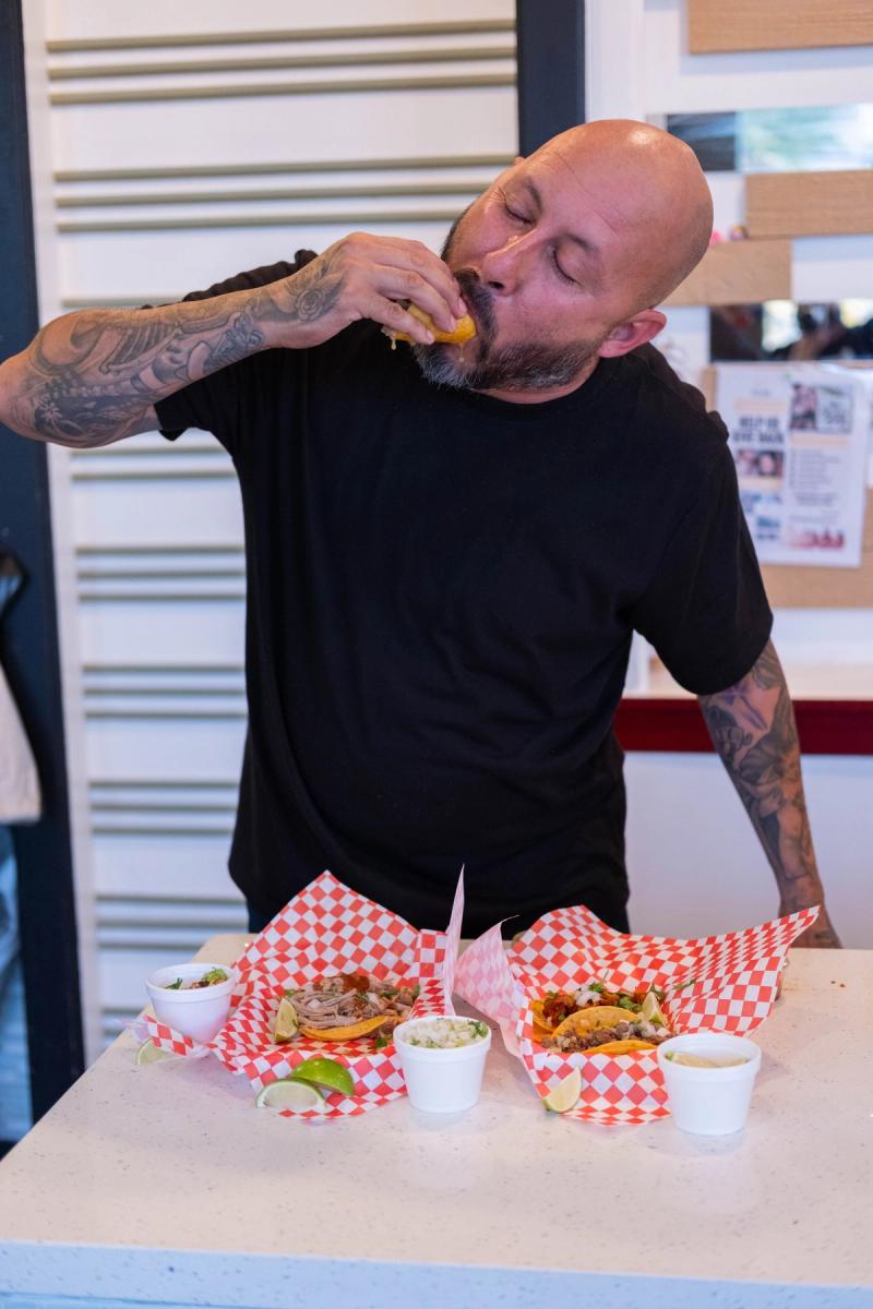 Owner taking a big bite of a taco behind the counter