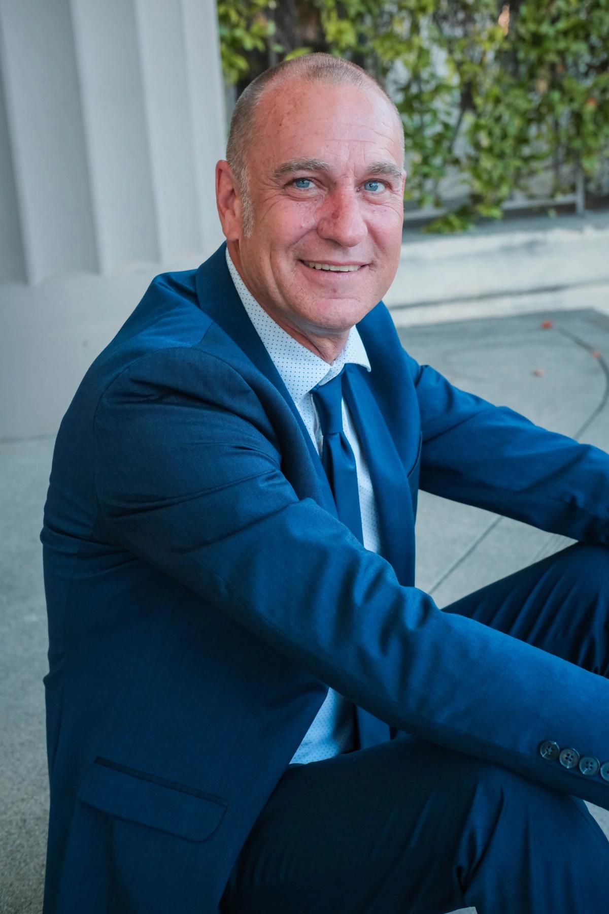 Smiling candidate in a blue suit seated on the steps of a civic building