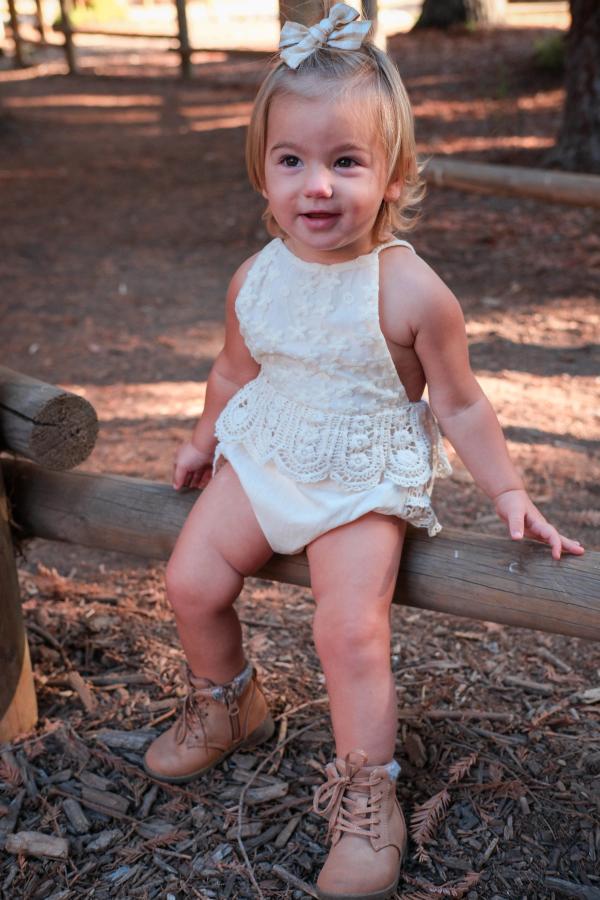 Toddler girl in a cream romper sitting on a log and looking up