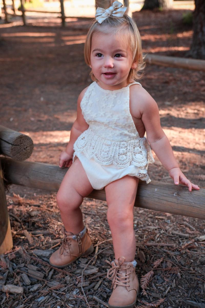 Toddler girl in a cream romper sitting on a log and looking up