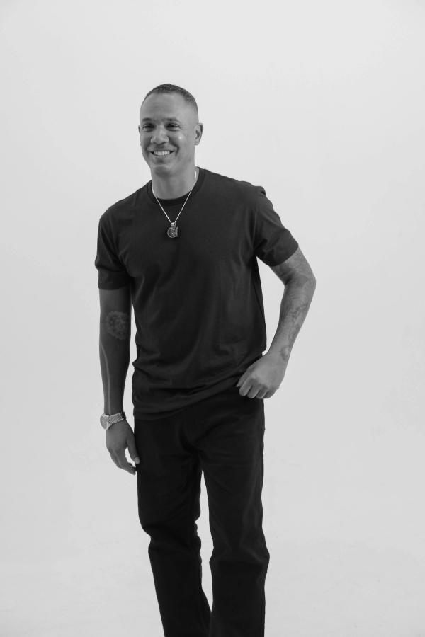 Man in a black T-shirt laughing with one hand in his pocket