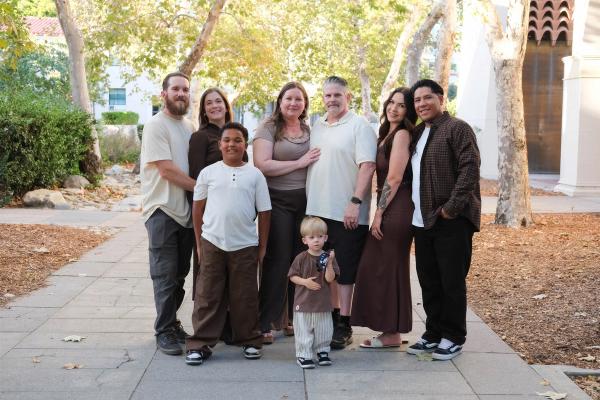 Three generations of a family of eight standing together on a tree-lined walkway in warm autumn light