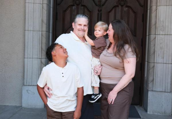 Grandparents laughing with a toddler on hip as their older grandson looks up and grins