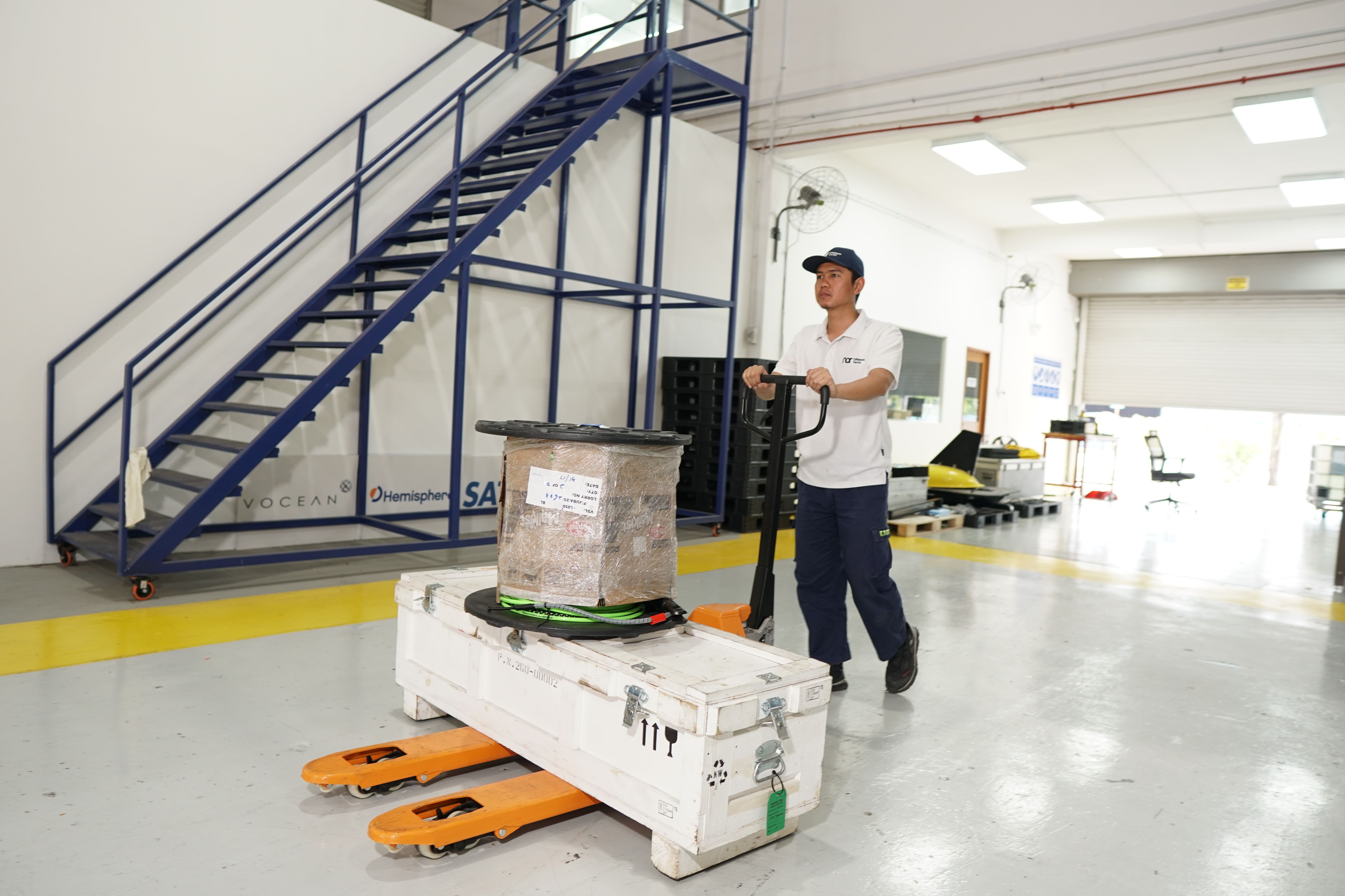 A man moves a large white container and package on an orange pallet jack in a warehouse.