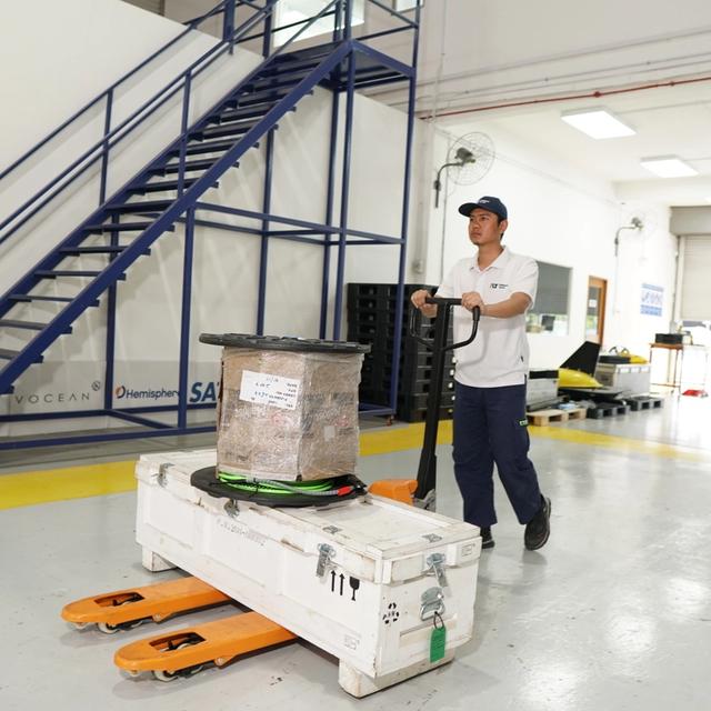 A man moves a large white container and package on an orange pallet jack in a warehouse.