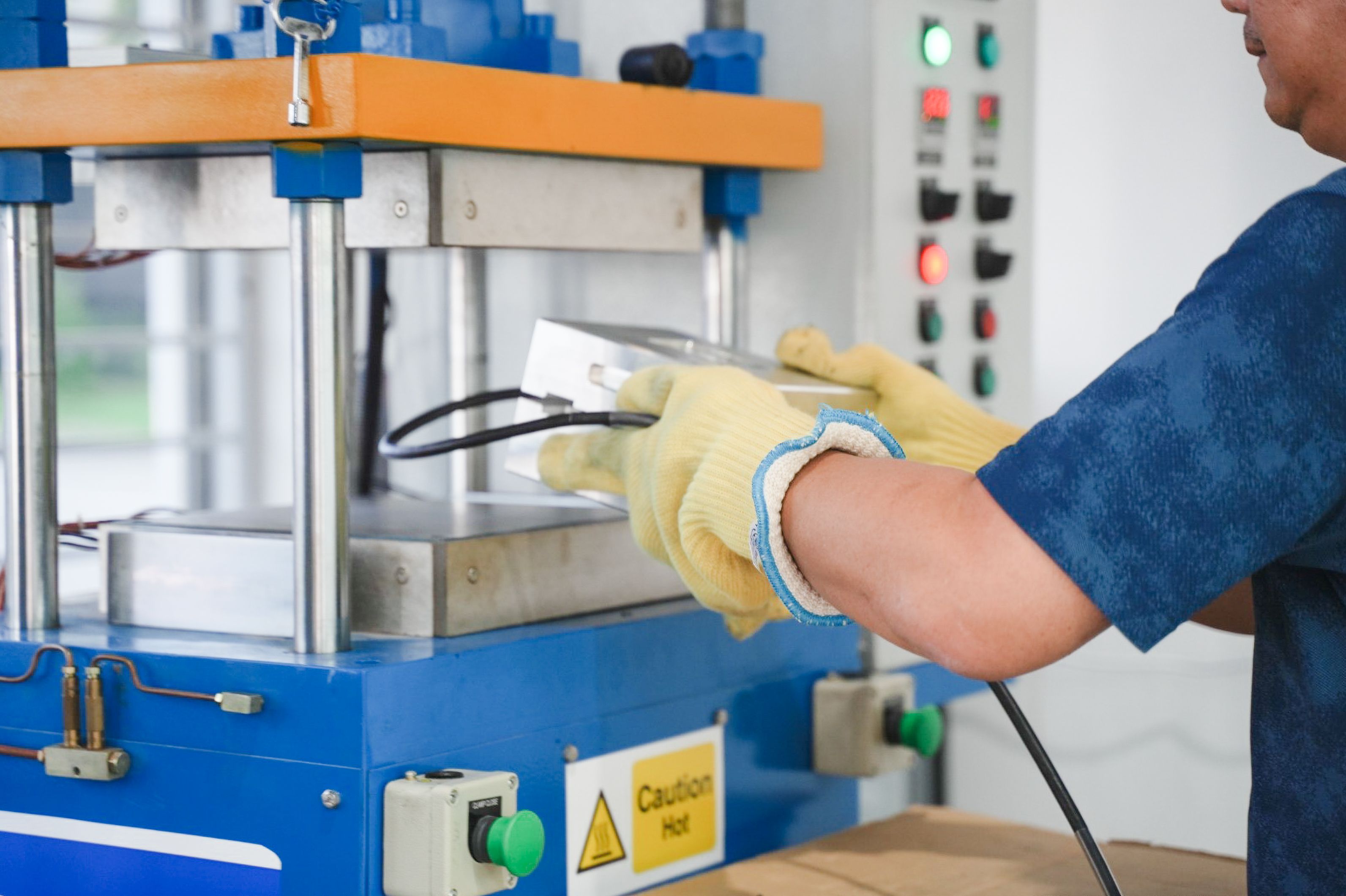 A person wearing yellow gloves uses a metal mold with an industrial heat press machine.