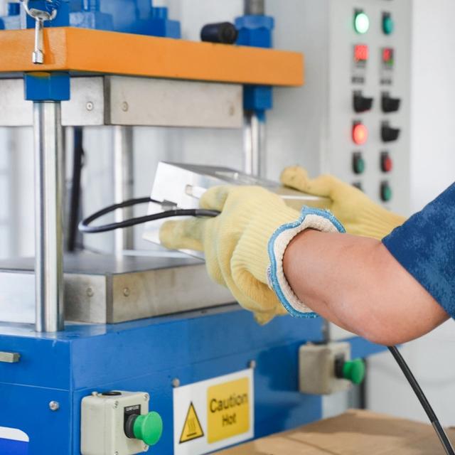 Worker in yellow gloves handling a metal part at an cable moulding machine.