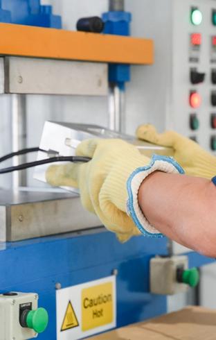 A person wearing yellow gloves uses a metal mold with an industrial heat press machine.