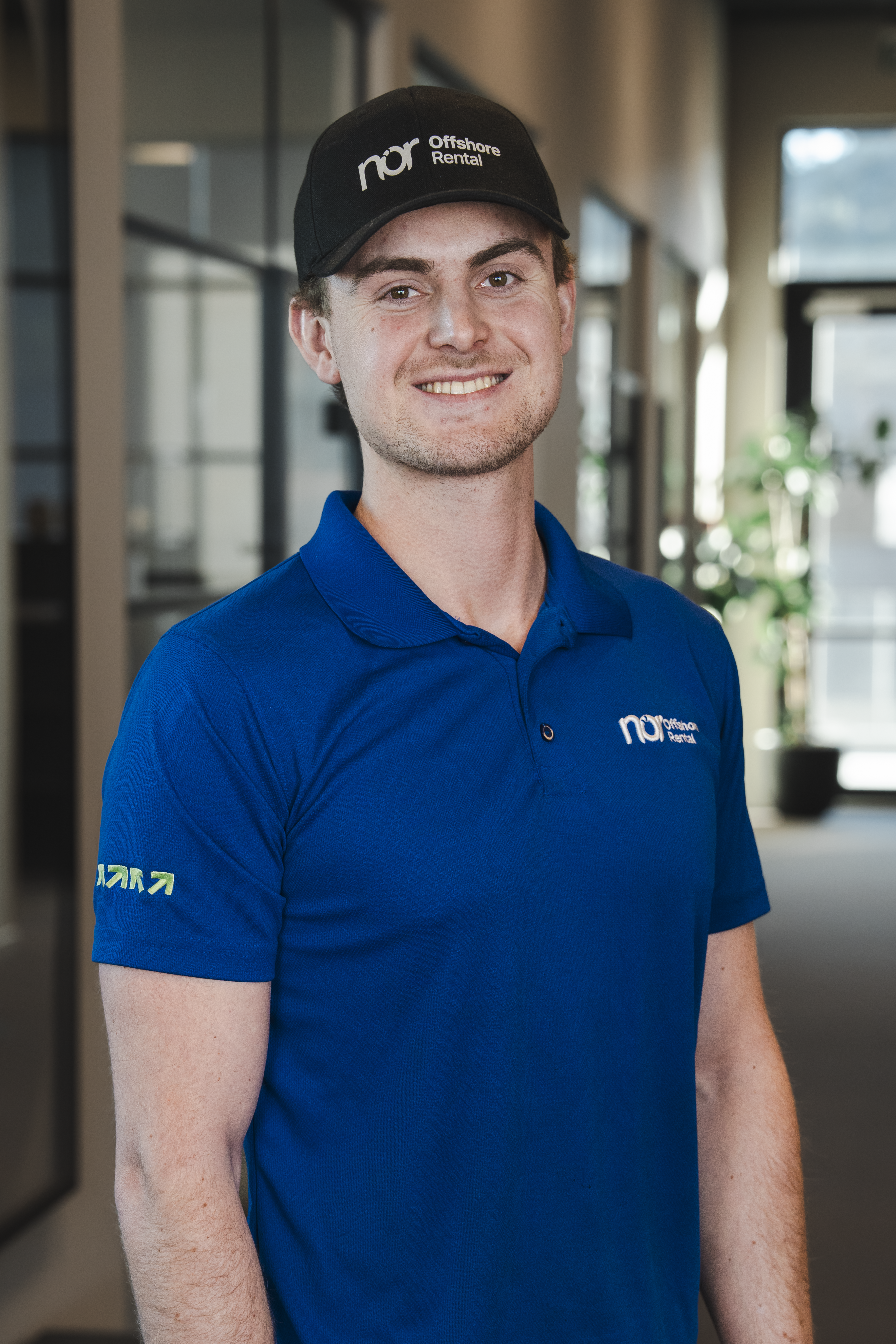 A smiling young man in a blue polo shirt and a black baseball cap with "nor Offshore Rental" logos.