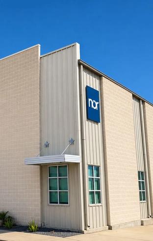 Beige building with corrugated metal siding, awnings, and a blue "nor" sign.