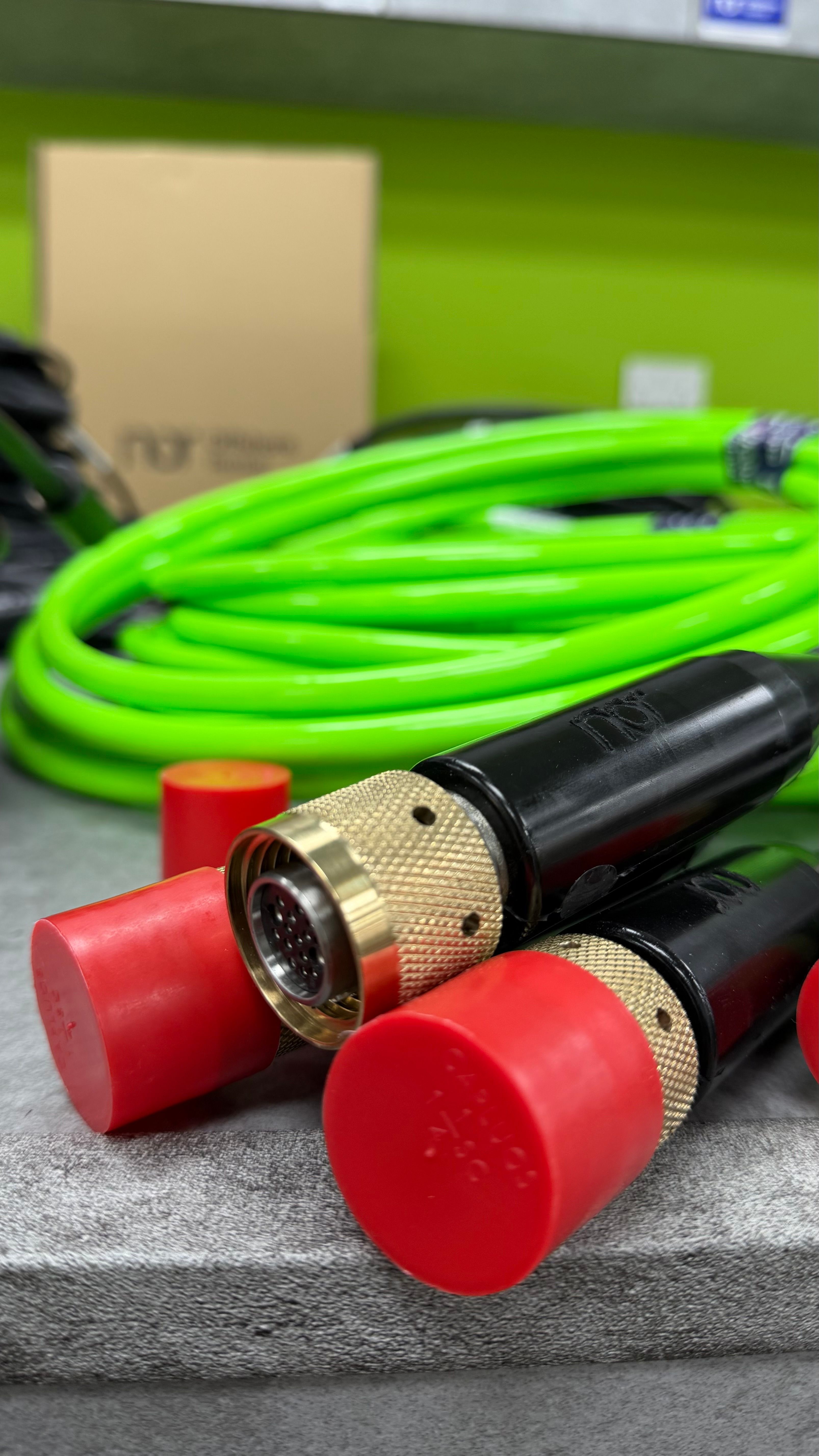 Two black connectors with brass fittings and red caps, with a coiled neon green hose in the background.