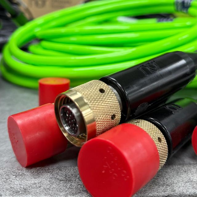 Two black connectors with brass fittings and red caps, with a coiled neon green hose in the background.