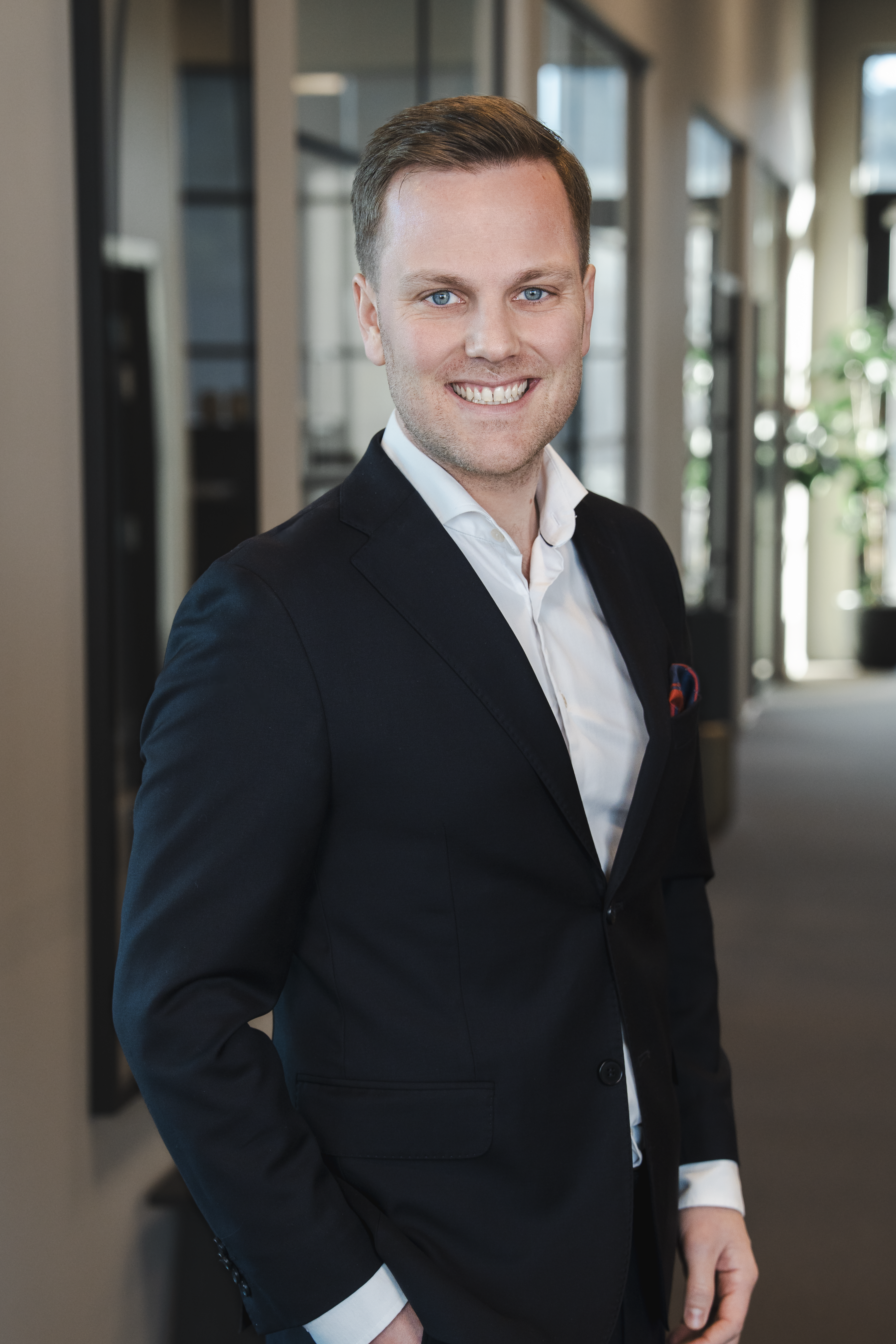 A smiling man in a suit stands in an office hallway.