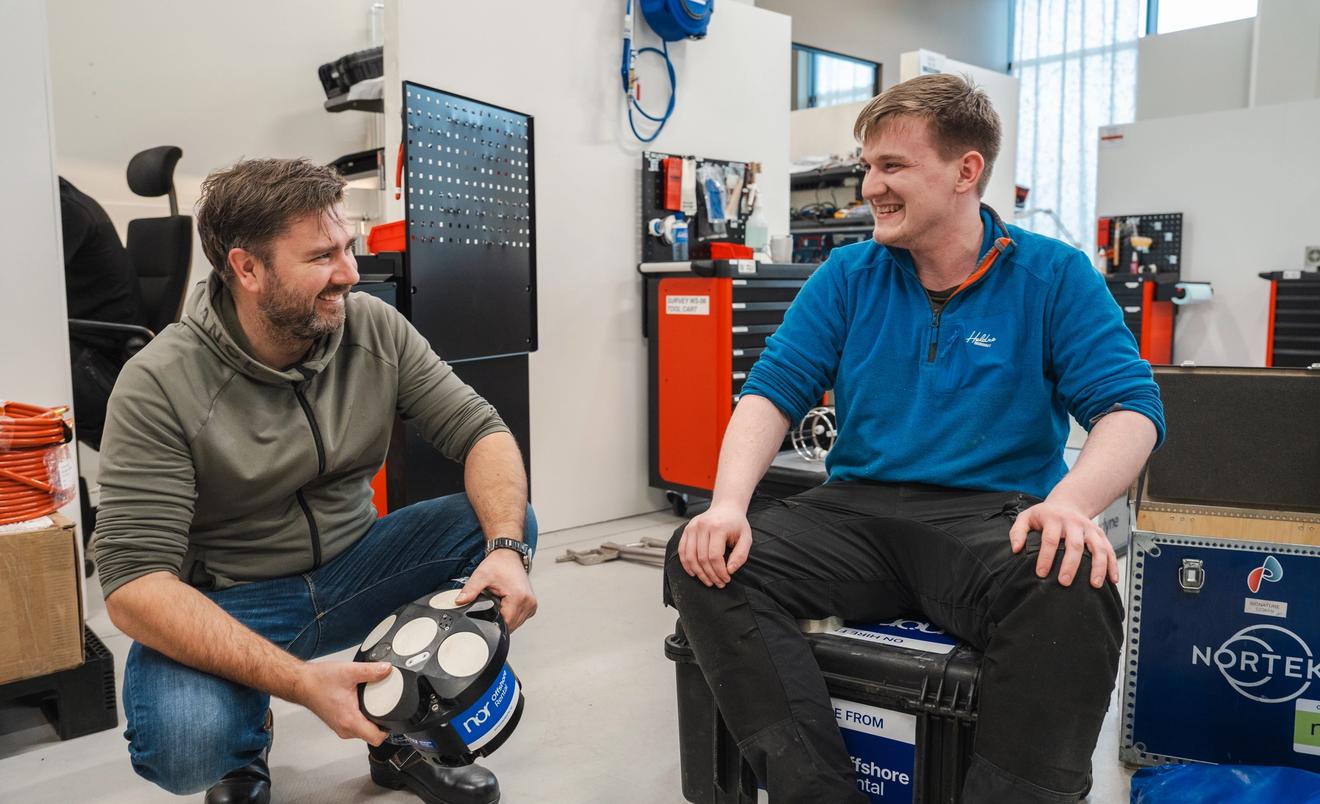 Two NOR employees smiling and talking in a workshop, surrounded by offshore rental equipment and tools.