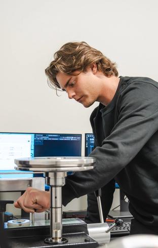 A young man operates lab equipment with computer monitors in the background.