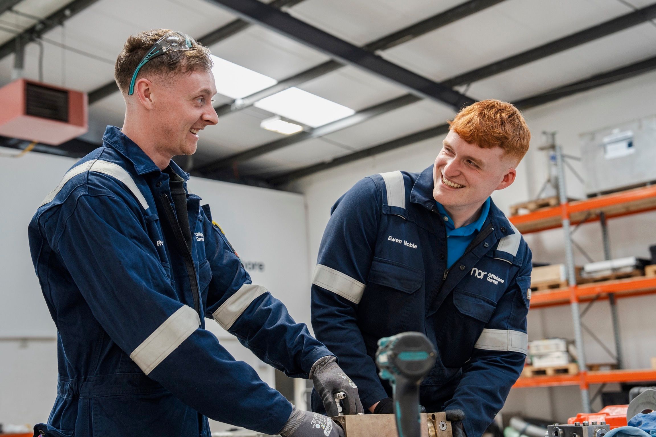 Two smiling workers in blue overalls conversing in a workshop.