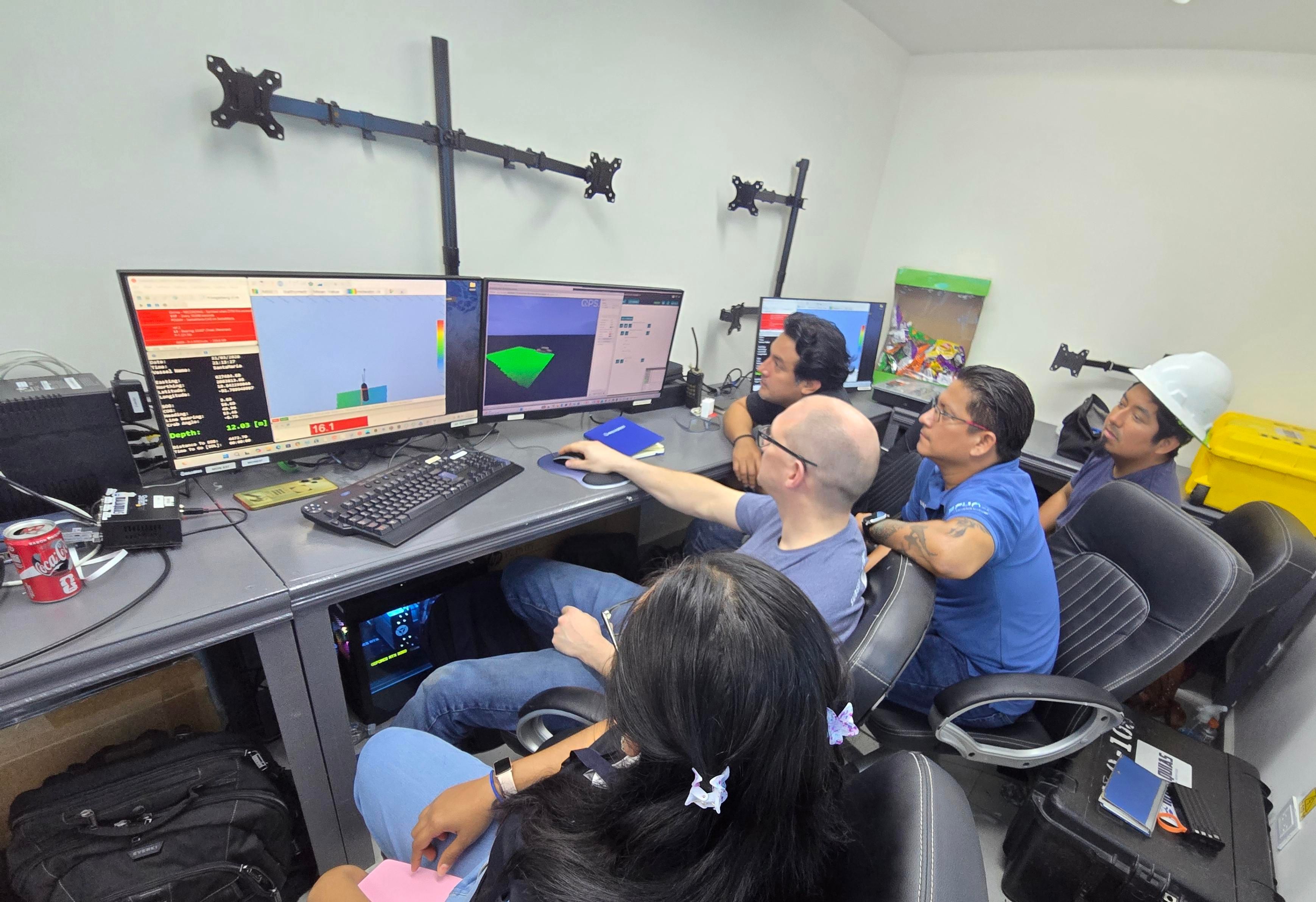 A diverse group of six people intently watches multiple computer screens displaying rocket simulations and data.