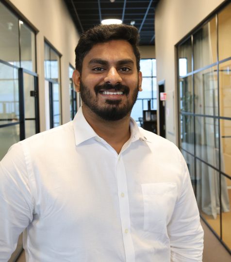 Smiling man in a white shirt with a beard in an office hallway.