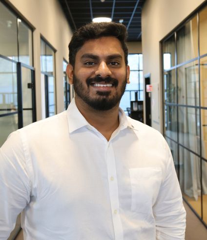 Smiling man in a white shirt with a beard in an office hallway.
