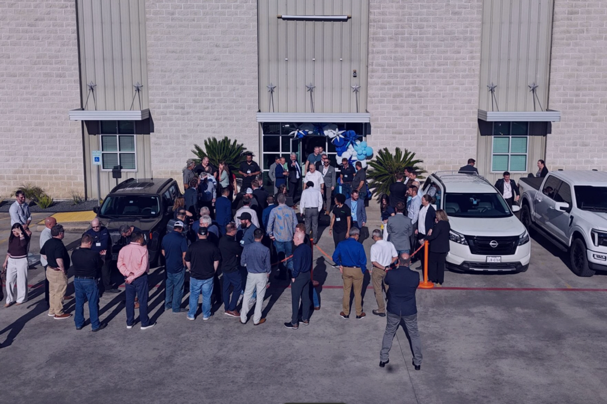 A crowd of people gathered outside a commercial building with cars and blue and white decorations.