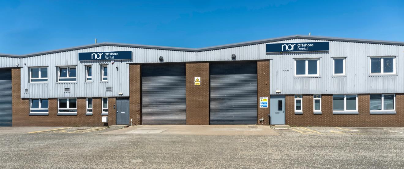 A grey corrugated metal and brick industrial building with "nor offshore rental" signs and multiple bay doors.